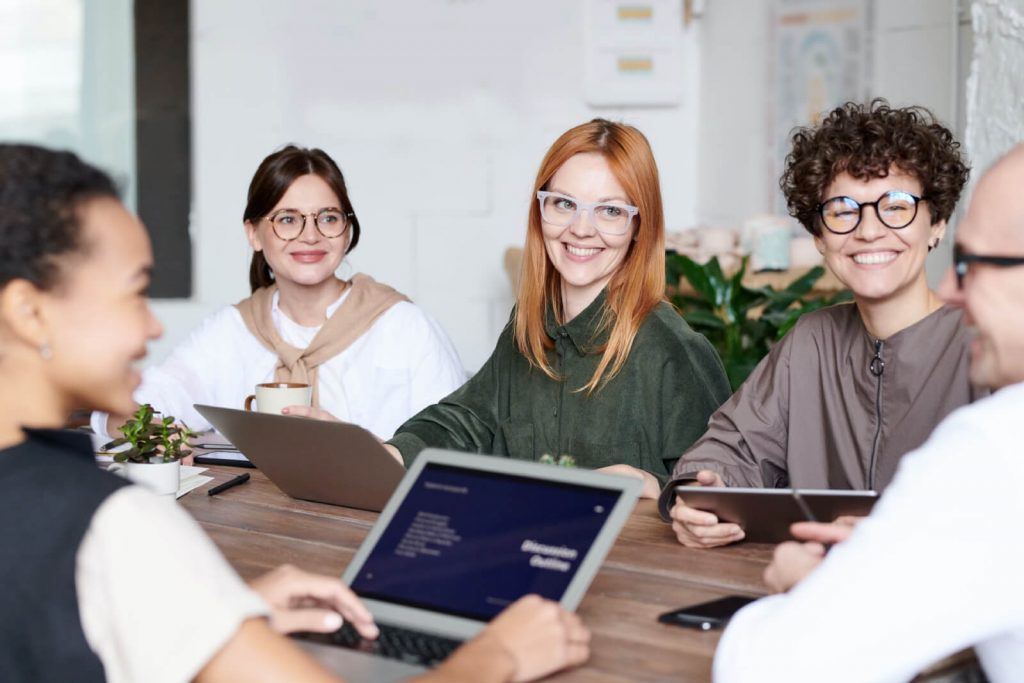 a group of people sitting around a table with laptops